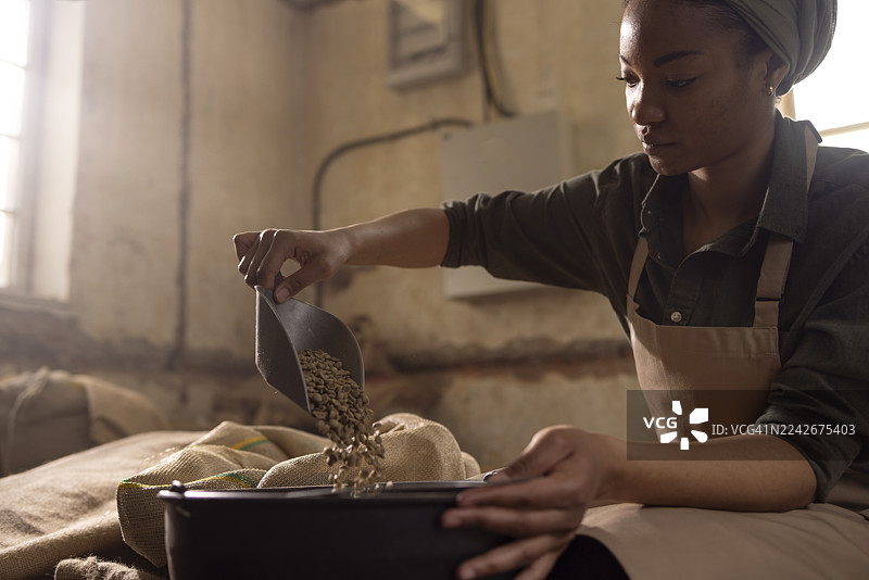 一位穿着围裙的女士正在乡村风格的工作室厨房里，将咖啡豆舀入一个大罐子里图片素材