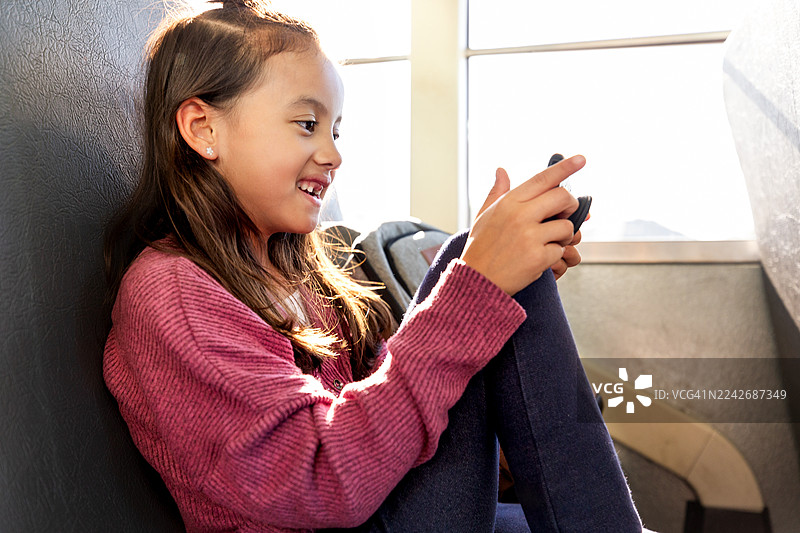 一个年轻女孩在光线明亮的房间里，微笑着看着她的便携式信息设备。图片素材