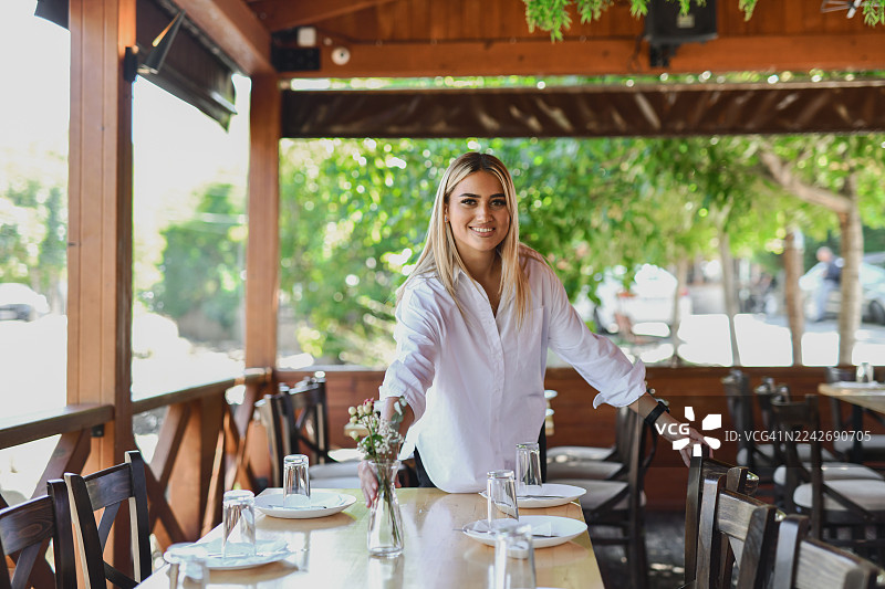 微笑的女服务员正在为优雅的露台用餐体验布置户外餐厅的餐桌图片素材