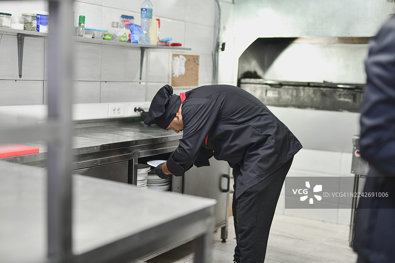 专业厨师在繁忙的厨房场景中，于不锈钢台面上准备餐盘图片素材