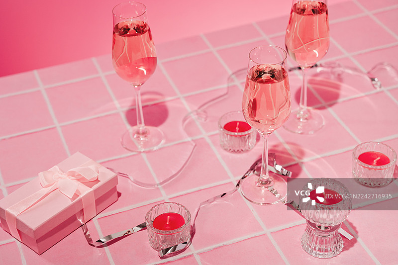 粉色瓷砖台面上的三个长笛玫瑰酒杯。俯视角度。桃红葡萄酒普罗塞克。茶蜡烛和礼品盒图片素材