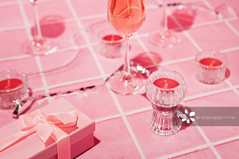 粉色瓷砖台面上的三个长笛玫瑰酒杯。俯视角度。桃红葡萄酒普罗塞克。茶蜡烛和礼品盒。图片素材