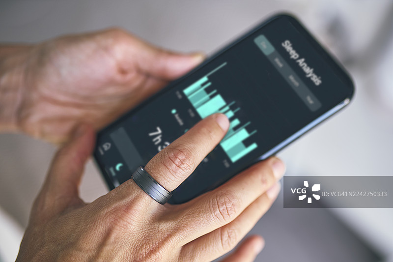 特写：在昏暗光线下，一只手拿着带有紫色应用程序界面的智能手机，手指上戴着一枚现代戒指图片素材