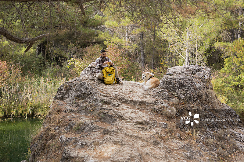 男人和狗在自然风光中徒步，在岩石上休息图片素材