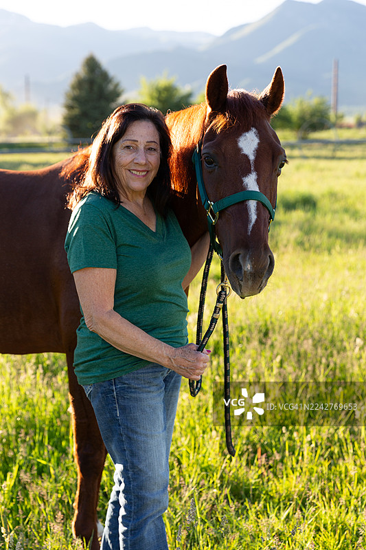 微笑的女士侧身站立在田野中，手牵着马的缰绳，犹他州海伯市，美国图片素材