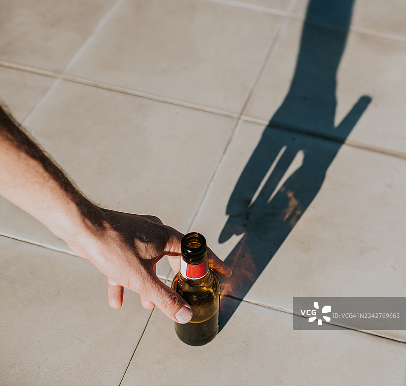 一只手伸向啤酒瓶，在地上投下阴影图片素材