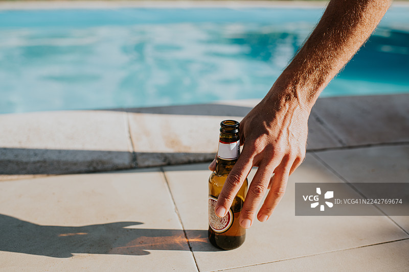 一只手在泳池边伸手去拿啤酒瓶图片素材