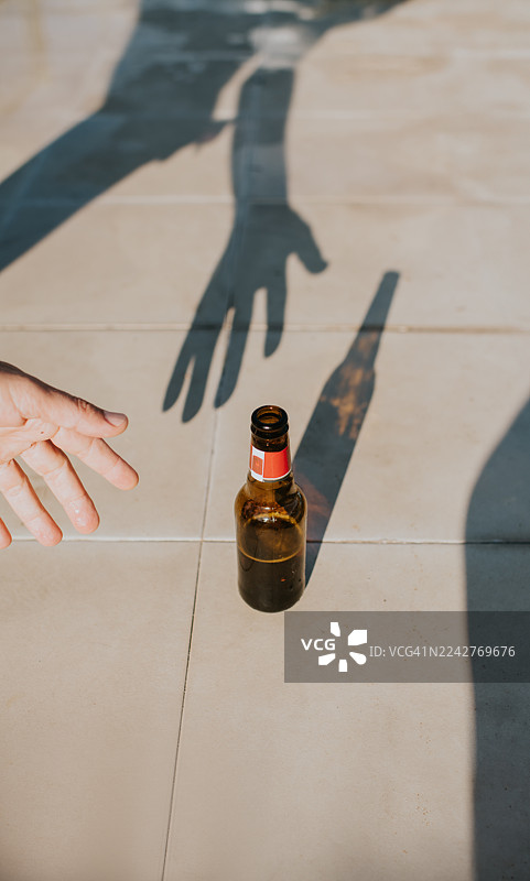 一只手伸向一个啤酒瓶，投下长长的影子图片素材