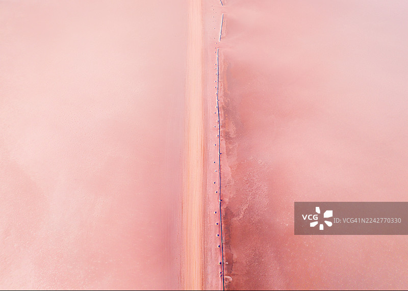澳大利亚维多利亚州马利地区，蒂勒尔湖附近，无人机从空中俯瞰笔直的土路和老旧的栅栏线穿过干燥的粉彩粉色盐沼的抽象景象图片素材