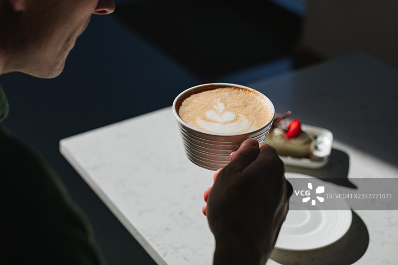 咖啡馆里，男人特写镜头，他正享用着一杯卡布奇诺和一块草莓芝士蛋糕图片素材