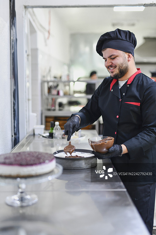 快乐的厨师在现代厨房工作室装饰巧克力甜点，工作时面带微笑图片素材