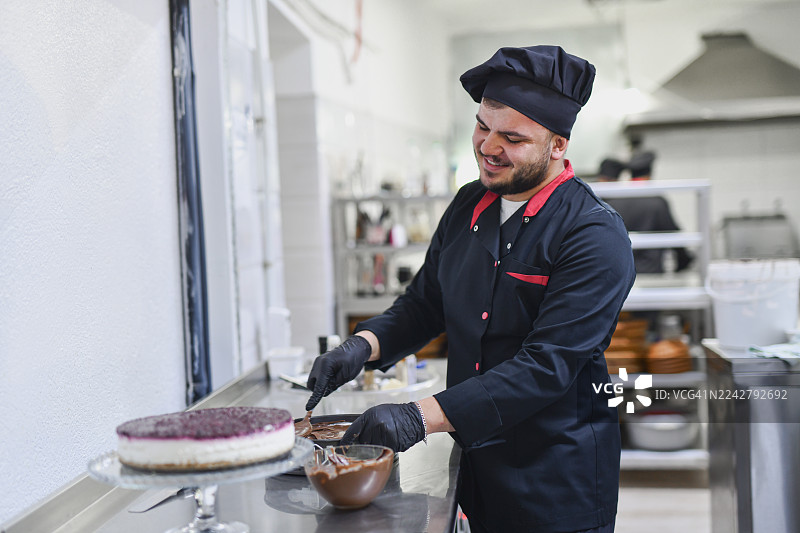 身着黑色制服的厨师在现代厨房工作室装饰巧克力蛋糕图片素材