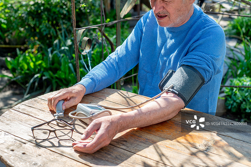 一位老年男子正在使用自动血压计测量他的血压图片素材