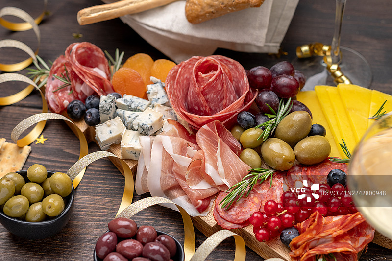 一个精致的熟食板，上面摆放着各种肉类、奶酪、水果和饼干，为节日庆典精心布置，旁边还有饮品和装饰品。图片素材