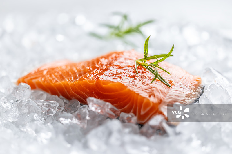 一块鲜橙色的生三文鱼柳，优雅地摆放在铺满碎冰的盘子上，鱼身上点缀着一小枝迷迭香，为这道菜增添了清新的草本风味。图片素材