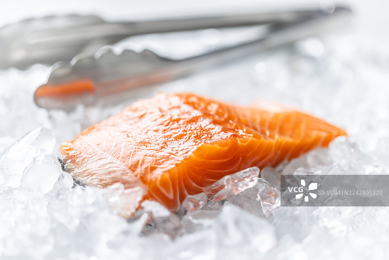 新鲜的三文鱼放在装满碎冰的白盘子里。三文鱼鲜亮的橙色与冰冷背景形成对比，旁边点缀着一小枝迷迭香，暗示着烹饪准备。图片素材
