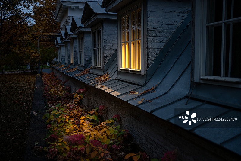 秋日阴云笼罩的傍晚，户外的花园里，一栋房屋的窗户透出温暖舒适的光芒，旁边是绣球灌木。图片素材