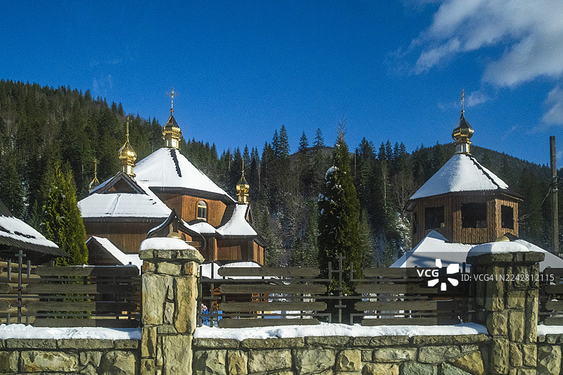 白雪皑皑的冬季，喀尔巴阡山脉的森林中，一座拥有金色圆顶的东正教木制教堂，传统宗教建筑在晴朗的蓝天下格外醒目。图片素材