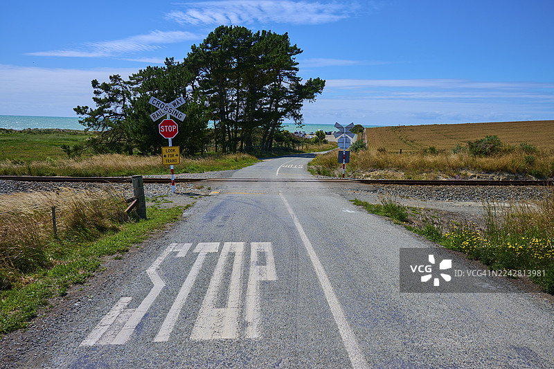 新西兰南岛蒂马鲁斯卡伯勒的乡村道路，设有停车标志和铁路道口，两侧为树木，远处为地平线。图片素材