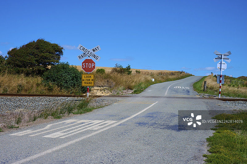 新西兰南岛蒂马鲁斯卡伯勒乡村道路上的铁路道口，有停车标志，周围环绕着自然风光和蓝天。图片素材