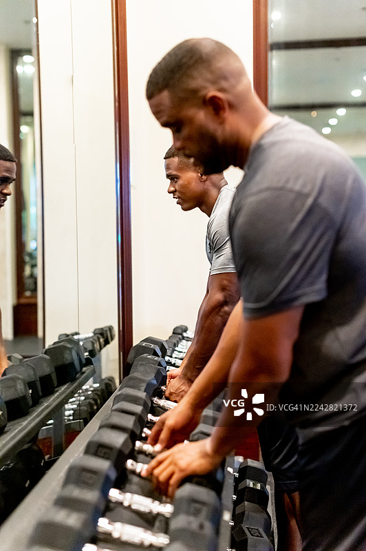 两位非裔美国男性，一位是父亲，另一位是成年儿子，在健身房一起锻炼，保持健康的生活方式，体现家庭团聚图片素材