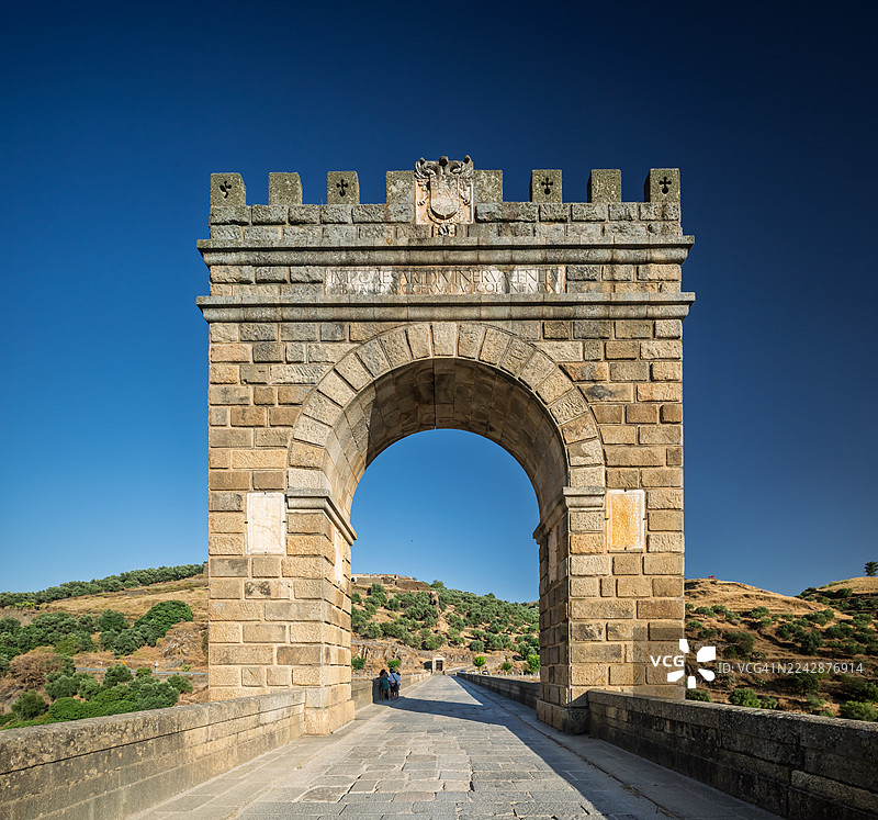 古罗马桥梁拱门，背景是晴朗的蓝天，远处的山丘和一条通往拱门下的小路，西班牙图片素材
