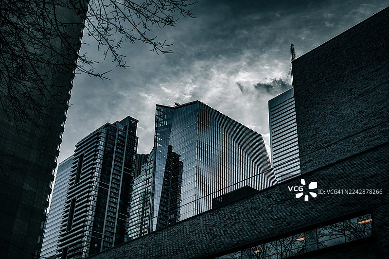 从低角度仰视现代建筑，背景是戏剧性的多云天空，展现了城市建筑和宏伟气势，多伦多，加拿大图片素材