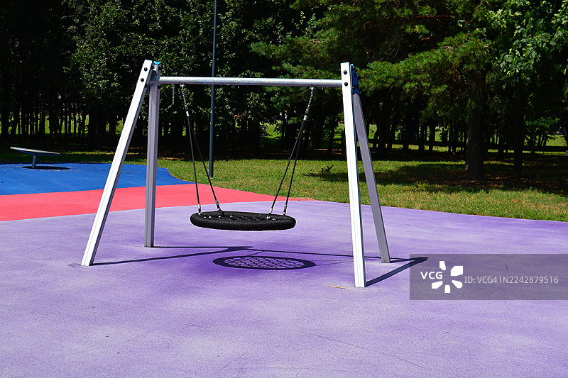 阳光明媚的日子里，色彩斑斓的游乐场里有秋千在空荡荡地荡着，周围环绕着绿色的树木图片素材