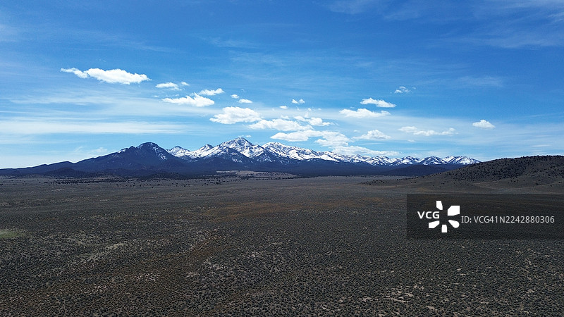 广阔的干旱地貌景观，远眺白雪皑皑的山脉，点缀着稀疏云彩的湛蓝天空，展现大自然的壮丽，尤里卡，美国图片素材