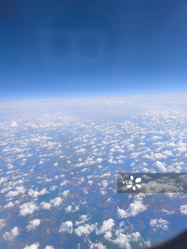 从飞机窗户看到的保加利亚布尔加斯的景象：蔚蓝的天空中飘着蓬松的白云，下方是拼布般的田野。图片素材