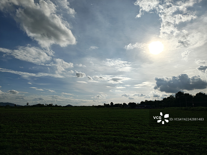 广阔的绿野，衬托着戏剧性的天空，阳光与云彩交织，构成一幅宁静而自然的风景画。图片素材
