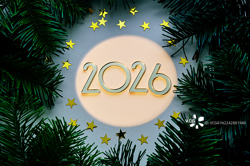 金色的数字2026，周围环绕着节日气氛的绿色松枝和闪亮的星星纸屑，象征着新年庆典和未来前景图片素材