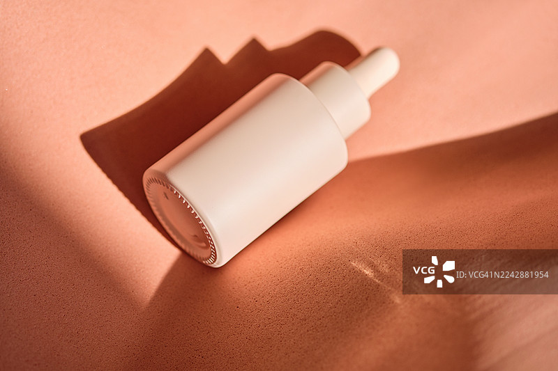 俯视视角，一瓶化妆滴管瓶置于带有粗糙阴影的纹理桃色背景上图片素材