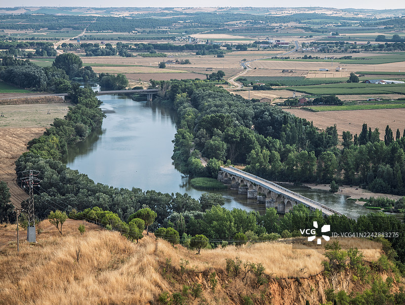 俯视河水蜿蜒流过郁郁葱葱的绿色山谷，其间点缀着桥梁和农田，天空布满云彩，地点：西班牙托罗（Toro）图片素材