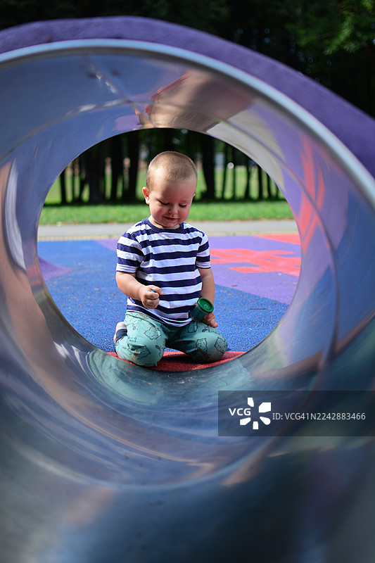 阳光明媚的日子里，一个快乐的小男孩在色彩鲜艳的游乐场滑梯上玩耍图片素材