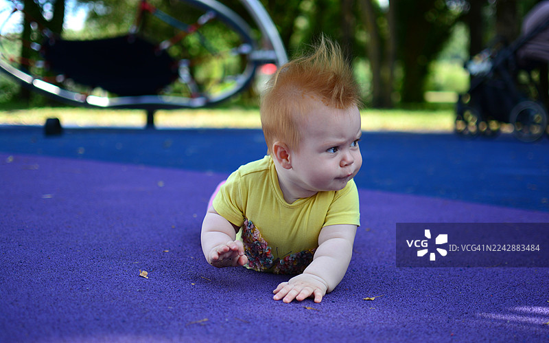 一个可爱的宝宝留着莫西干发型，在户外的紫色游乐场地上爬行图片素材
