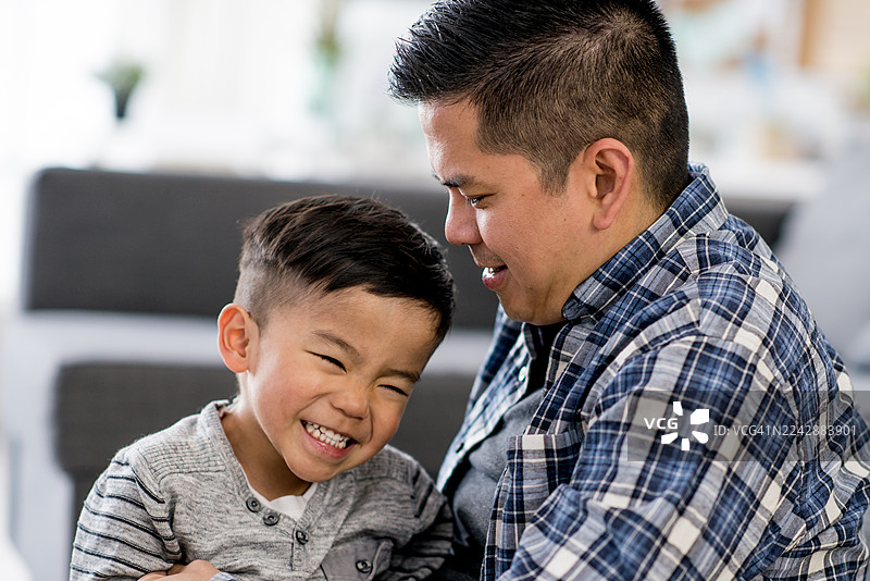 温馨的居家时刻：父亲与儿子共享欢乐笑声，亚洲家庭肖像，情感联结图片素材