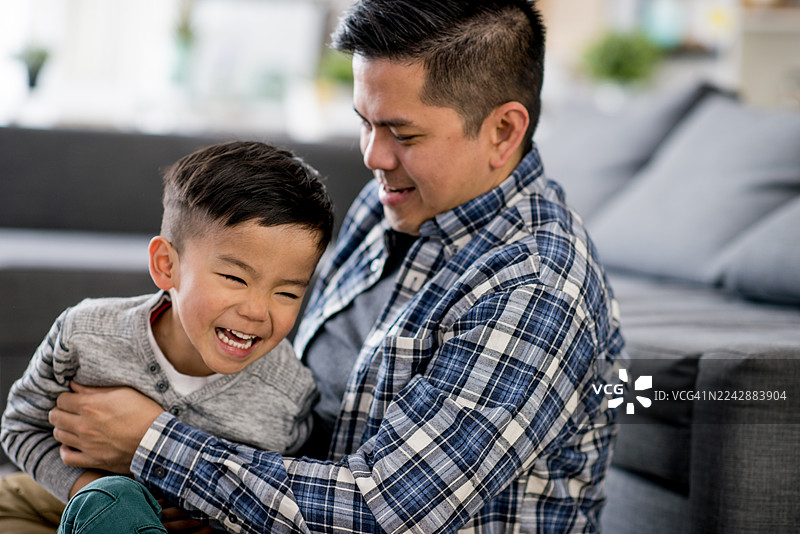 亚洲父亲在家中与儿子欢笑，温暖的拥抱突显家庭的亲情与喜悦图片素材