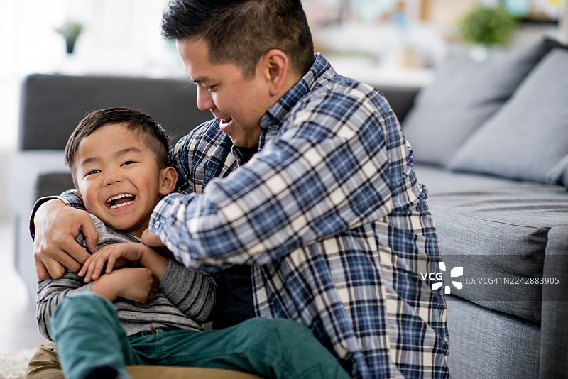 亚洲父亲和儿子在舒适的家中客厅地板上一起大笑图片素材