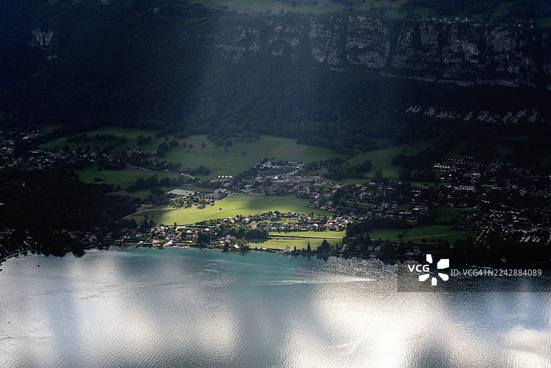 从高处俯瞰湖泊和坐落在山谷中的村庄，阳光照亮了部分风景，法国，福尔克拉兹山口图片素材