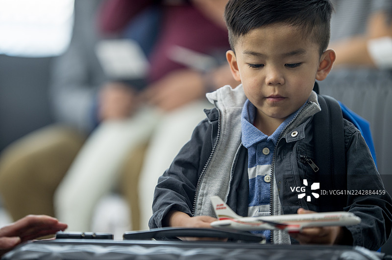 年轻的亚裔男孩在机场，在旅行前玩着模型飞机玩具图片素材