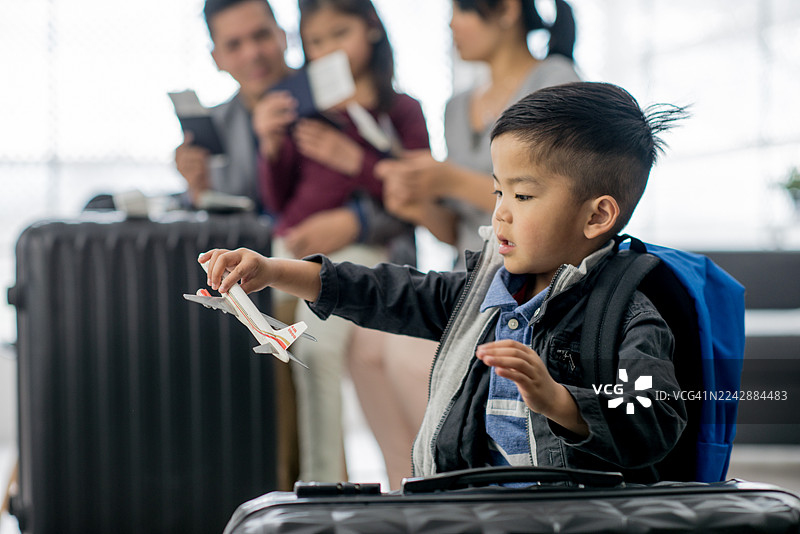 年轻的亚洲男孩在机场，手持玩具飞机，周围是家人和行李图片素材