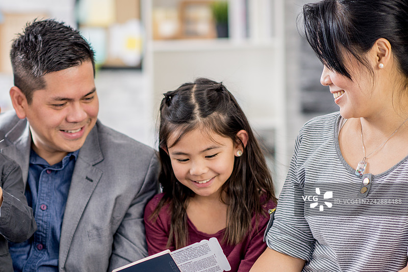 全家共享阅读时光：幸福的亚洲父亲、女儿和母亲在家中温馨相聚图片素材