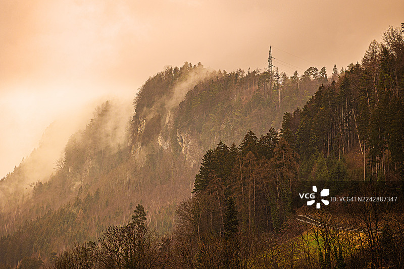 橙色天空下的山坡上的雾气森林和电线塔，奥地利费尔德基希图片素材