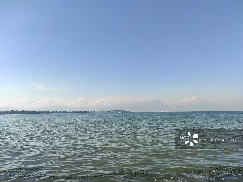 意大利西尔米奥内，圣玛丽亚迪卢加纳公共海滩，晴朗蓝天下壮阔大海的风景，远处的山脉和海岸线清晰可见，营造出宁静与自然之美的氛围图片素材