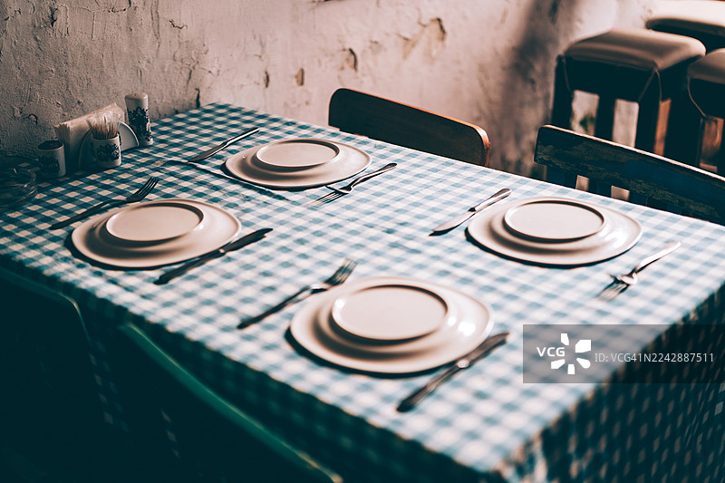 舒适的希腊小酒馆，质朴的餐桌布置，格子桌布和为四位客人准备的白色盘子图片素材