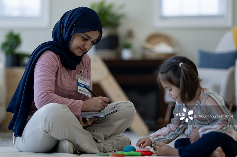 戴着头巾的南亚女性在家中指导孩子玩彩泥图片素材