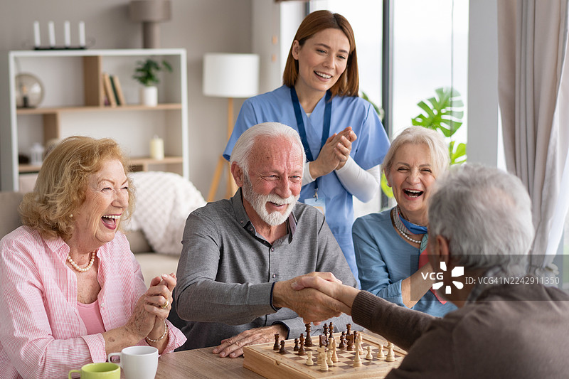 老人们在国际象棋比赛中开怀大笑，用力握手图片素材