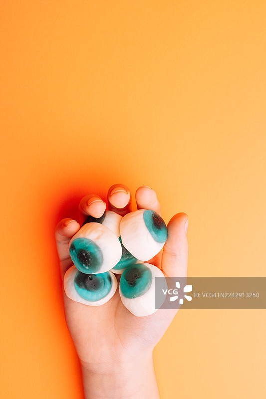 橙色背景上，手握着橡皮糖眼球图片素材