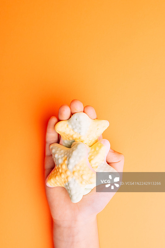 一只手拿着星星形状的软糖，背景为橙色图片素材